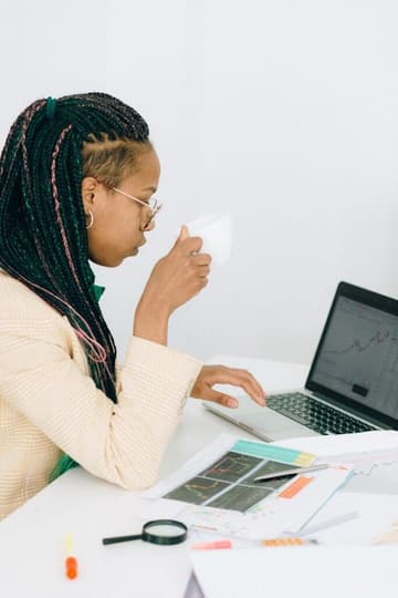 pexels-photo-7173020 A businesswoman with braided hair analyzing stock charts on a laptop, holding a cup.